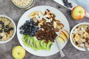 Cooking breakfast. Cooked oatmeal and a plate with dried fruits, nuts, fruits and berries on a gray background. photo