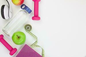 Two red dumbbells, an apple, a tape measure, a bottle of water and weight scales on a white background. Concepts about fitness, sport and health. Copy space for text. Home workout concept photo