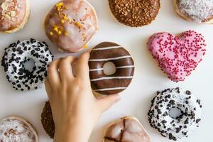 Hand reaches for a donut with chocolate. Donuts with colored icing on a white background. photo