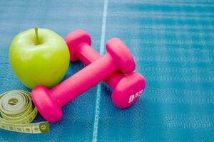 dos rojo mancuernas, un manzana y un centímetro cinta en un yoga estera. conceptos acerca de aptitud física, deporte y salud. foto