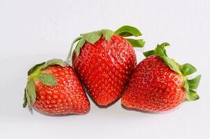 Tres fresas son mostrado en un blanco superficie foto