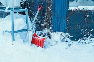 Red shovel for removes snow from the road and clears the sidewalk in winter season. Cleaning and clearing roads after snowfalls and blizzards photo