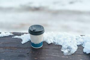 disposable coffee cup on the snow, Cardboard hot Tea Cup in winter season. Takeaway beverage photo