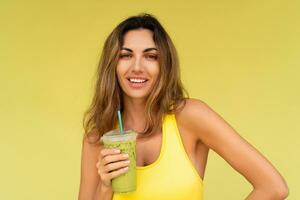 Studio photo of pretty brunette woman in sportive outfit  hoding beverage and posing on yellow background. Perfect slim body.