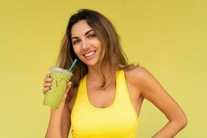 Studio photo of pretty brunette woman in sportive outfit  hoding beverage and posing on yellow background. Perfect slim body.