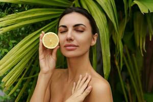 Beautiful woman holds lemons. Photo of attractive woman with perfect makeup on   green palm trees  background. Beauty concept
