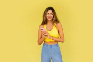 Pretty brunette woman posing with mobyle phone  over yellow background. Casual stylish outfit. photo