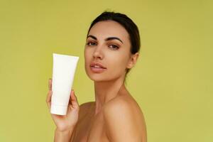 Smiling woman holds tube with cosmetic cream. Photo of attractive woman with perfect makeup on  yellow  background. Beauty concept