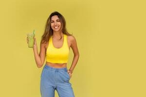 Studio photo of pretty brunette woman in sportive outfit  hoding beverage and posing on yellow background. Perfect slim body.