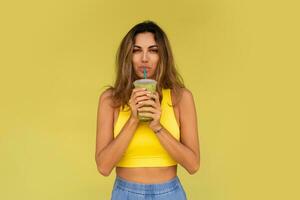 Studio photo of pretty brunette woman in sportive outfit  hoding beverage and posing on yellow background. Perfect slim body.
