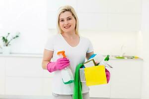 Cropped image of beautiful woman in protective gloves holding a flat wet-mop and bucket with detergents and rags while cleaning her house photo