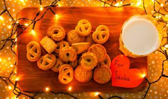 Wooden board with yellow cookies, glass of milk, paper heart For Santa and surrounded with Christmas lights photo