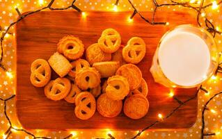 Glass of milk on the wooden board with cookies and Christmas lights photo