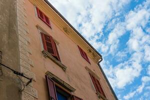 Unusual look at the old italian building with closed window shutters and blue cloudy sky on the background photo