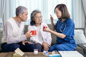 Senior couple get medical advice visit from caregiver nutritionist at home while having suggestion on herbal hot chamomile tea drink for longevity, healthy sleep and cure to insomnia photo