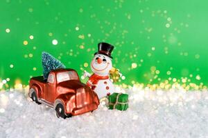 Christmas card with space for text with a red pickup truck and a Christmas tree in the back, a cheerful snowman on a green background with blurry bokeh photo