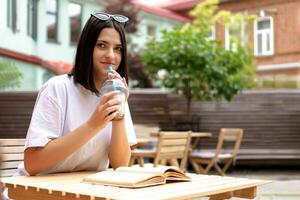 un linda morena niña es sentado a un mesa en un verano restaurante con un enfriamiento bebida foto