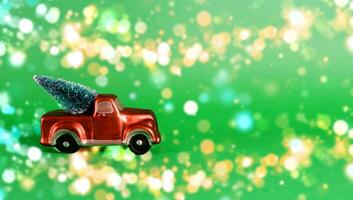 New Year card with place for text. Red car with a Christmas tree in the back of a pickup truck on a green background with blurry bokeh photo