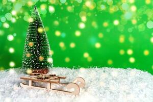 Artificial Christmas tree with wooden sleigh on artificial snow on a green background with blurry bokeh. Merry Christmas and Happy New Year greeting card photo