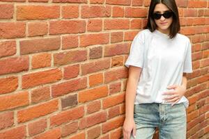 Summer portrait of a brunette girl in sunglasses against a brick wall with a place for text. City life concept photo
