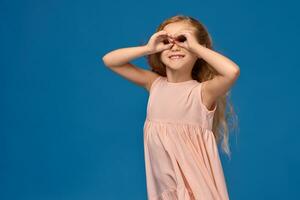 Fashionable little girl in a pink dress is posing on a blue background. photo