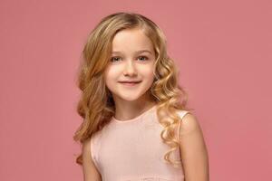 Little girl with a blond curly hair, in a pink dress is posing for the camera photo