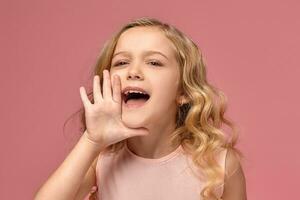 pequeño niña con un rubio Rizado cabello, en un rosado vestir es posando para el cámara foto