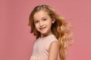 Little girl with a blond curly hair, in a pink dress is posing for the camera photo