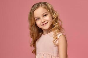 Little girl with a blond curly hair, in a pink dress is posing for the camera photo