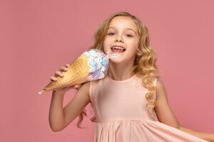 pequeño niña con un rubio Rizado cabello, en un rosado vestir es posando con un helado foto