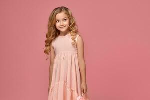 Little girl with a blond curly hair, in a pink dress is posing with a candy photo