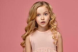 Little girl with a blond curly hair, in a pink dress is posing for the camera photo