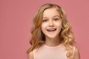 Little girl with a blond curly hair, in a pink dress is posing for the camera photo