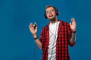 Happy young man listening to music with headphones. Handsome smiling guy in checkered shirt dancing and singing with headphones. photo