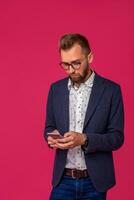 Studio shot of attractive brunette business man with glasses, in casual shirt, stylish black jacket holding a smartphone photo