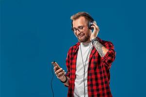 Happy young man listening to music with headphones. Handsome smiling guy in checkered shirt dancing with headphones. photo