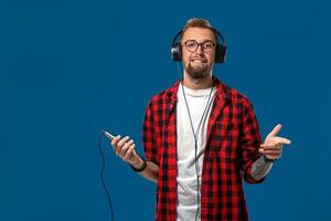 hermoso joven elegante hombre en auriculares participación mp3 jugador y bailando mientras en pie en contra azul antecedentes foto