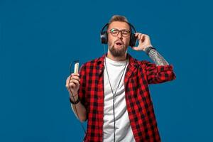 Happy young man listening to music with headphones. Handsome smiling guy in checkered shirt with closed eyes dancing with headphones. photo