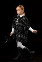 Little girl in a dark poncho, black boots and a clutch in her hand photo