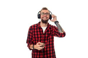 Young hipster man in checkered shirt and glasses wearing earphones looking happy on white background. photo