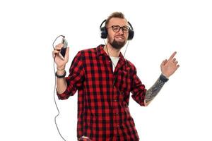 Young hipster man in checkered shirt and glasses wearing earphones looking happy on white background. photo