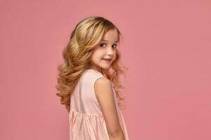 Little girl with a blond curly hair, in a pink dress is posing for the camera photo