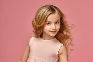 Little girl with a blond curly hair, in a pink dress is posing for the camera photo