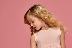 Little girl with a blond curly hair, in a pink dress is posing for the camera photo