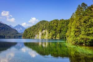 verde arboles reflejando en un calma plano agua de un montaña lago durante un caliente verano foto