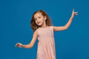 Fashionable little girl in a pink dress is posing on a blue background. photo