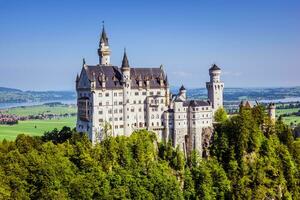Neuscwanstein castle on the mountain with green fields and blue sky on the background photo