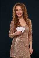 Beautiful young emotional woman in cocktail dress showing her cards to opponent, four of aces, best hand. Blcak background, studio shot photo