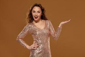 Portrait of a smiling woman in golden dress holding copyspace on the palm on a brown background photo