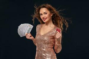 Image of lucky happy woman with brown long hair with fan of 100 dollar bills, lots of cash money, over black background photo